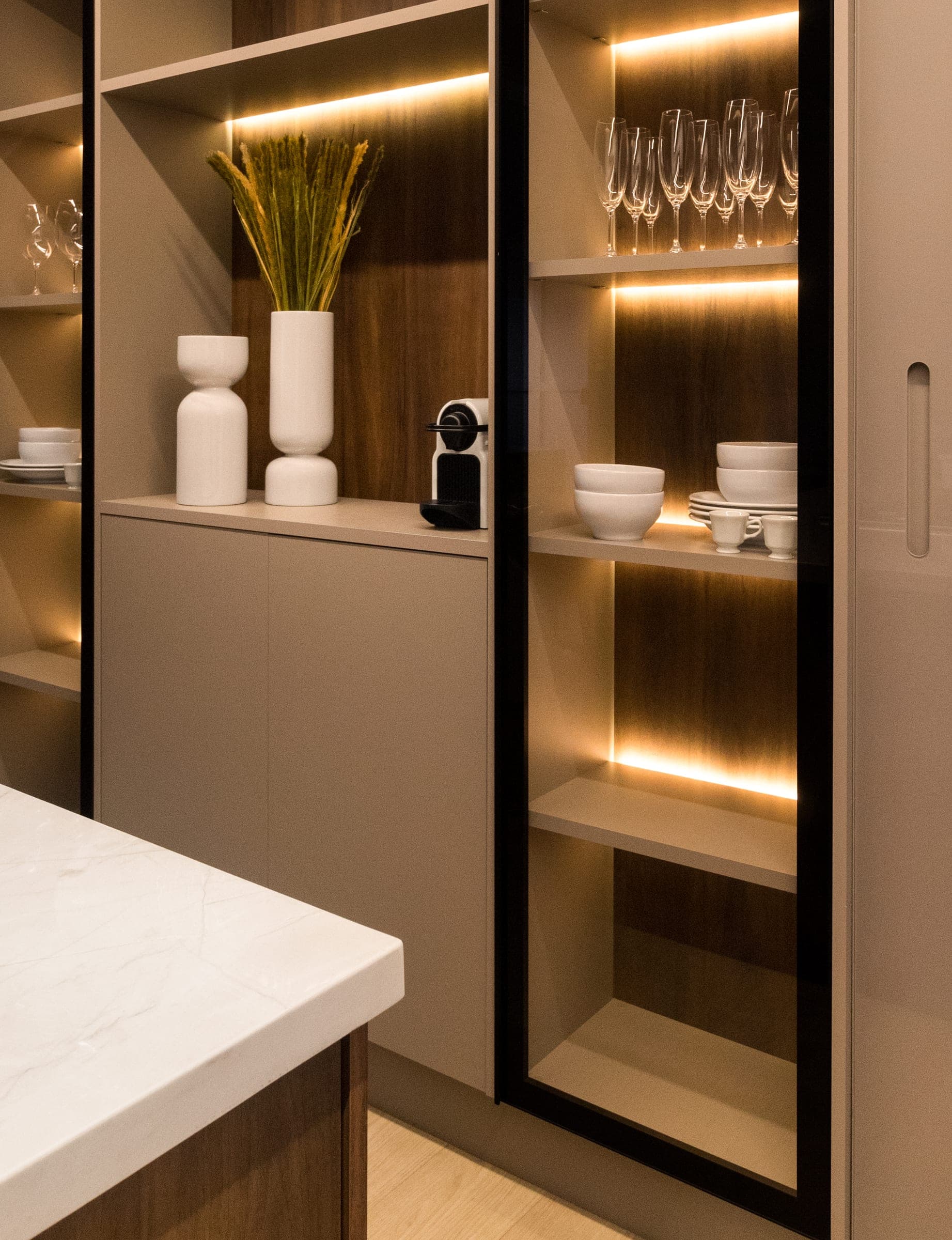 Cristaleira com porta de vidro de perfil preto, prateleiras iluminadas e fundo em nogueira