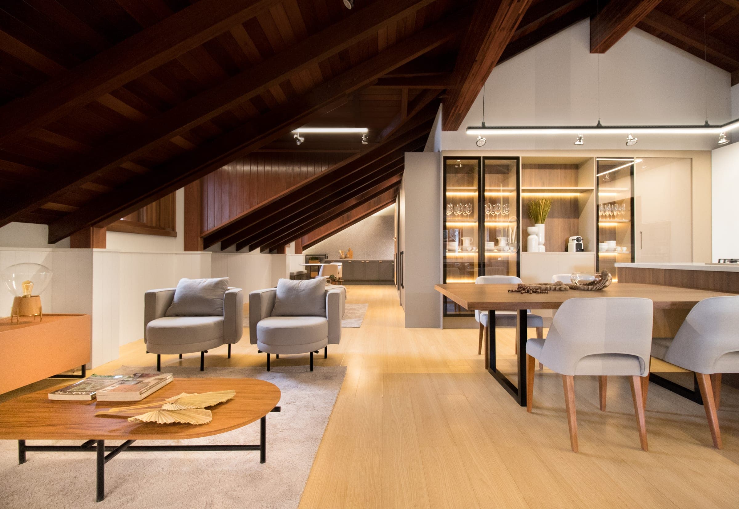 Ambiente integrado de estar e jantar com poltronas, mesa em nogueira e cristaleiras