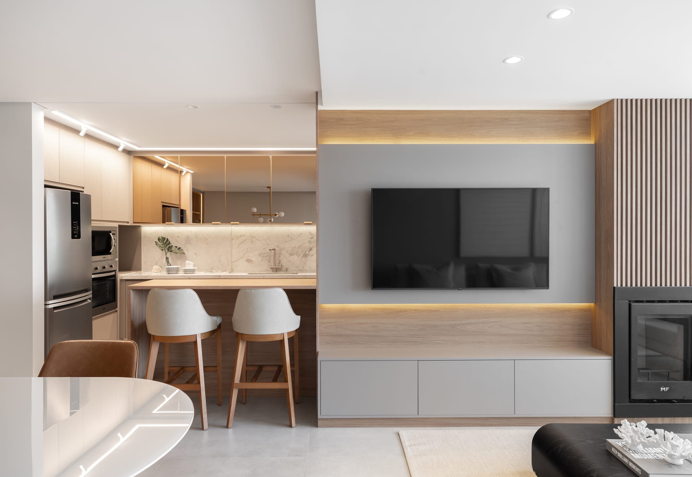 Estar e cozinha integrados com painel de TV, ilha gourmet e banquetas